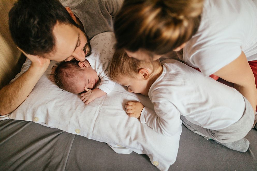 Eine Familie mit Baby liegt auf dem dem Bett