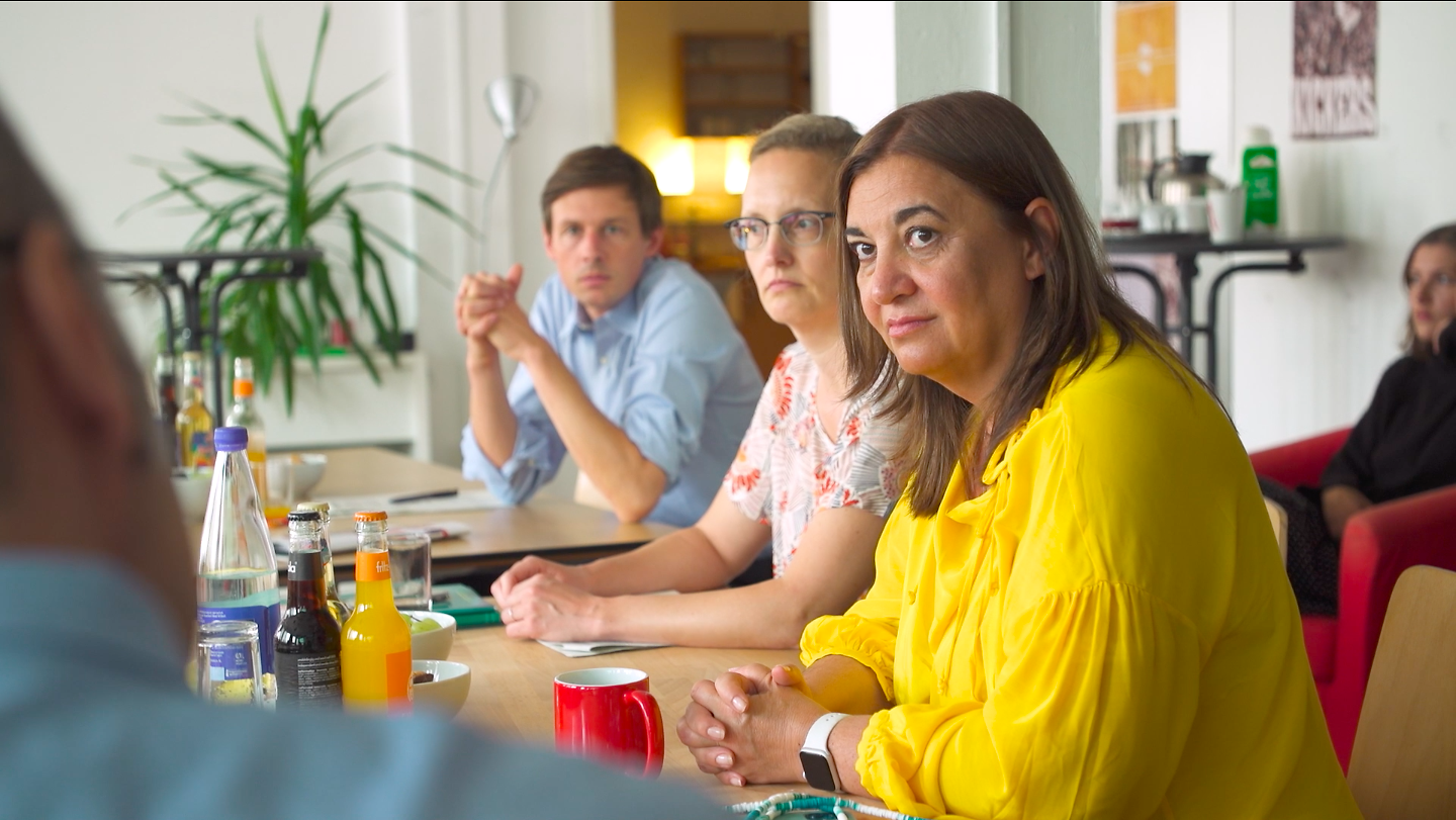 Frau Deligöz steht zwischen vielen Menschen in einem Hof und hält das Schild der Initiative "neue Chancen für Kinder" hoch