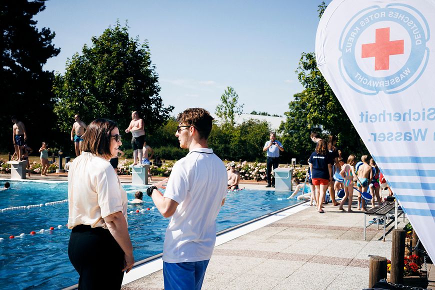 Ekin Deligöz steht vor einem Schwimmbecken im Freibad und unterhält sich mit einem Vertreter des Freibads