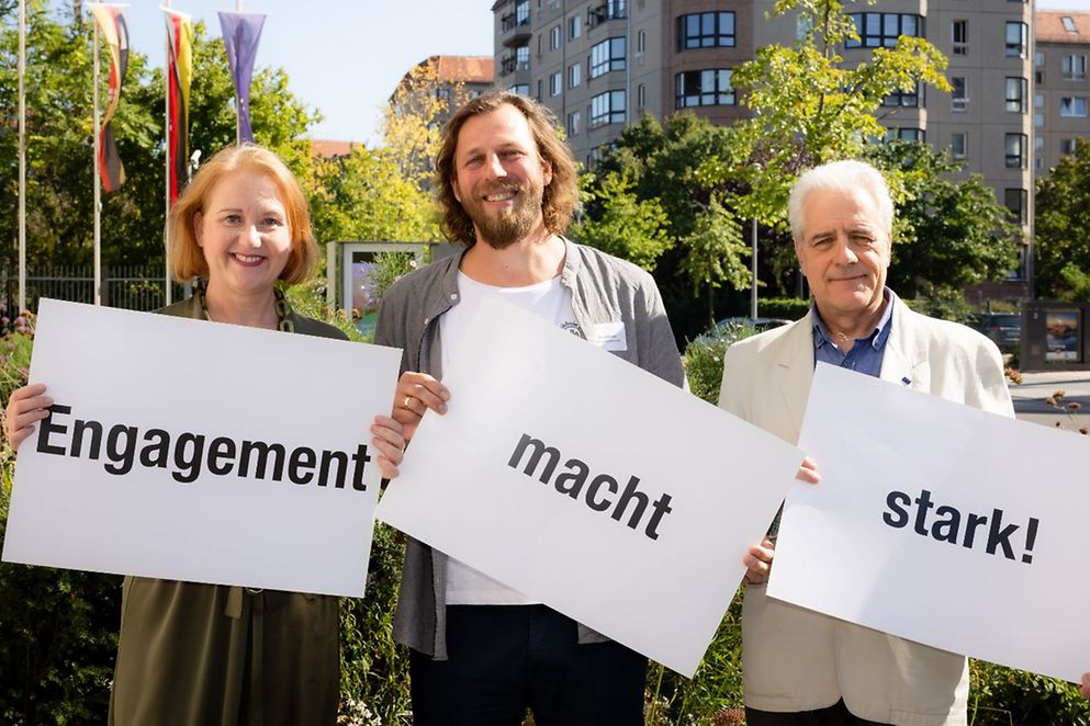 Bundesfamilienministerin Lisa Paus, Samuel Drews und Rainer Hub halten Plakate mit der Aufschrift "Engagement macht stark!".