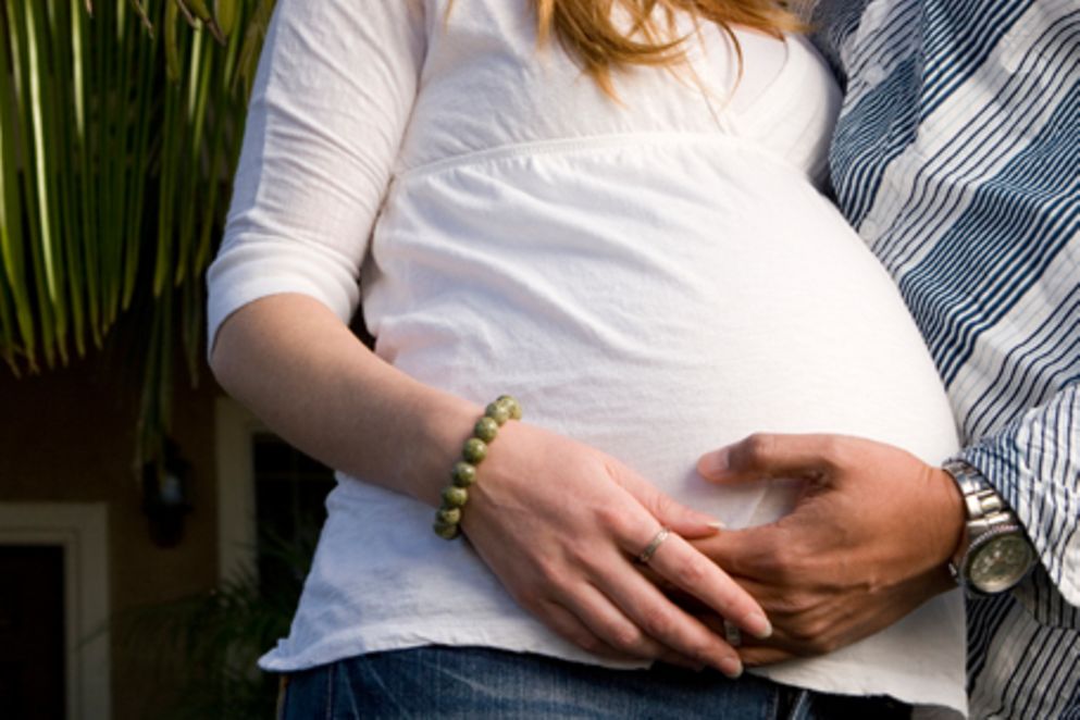 Eine Schwangere und eine Mann, der seine Hand auf ihren Bauch gelegt hat